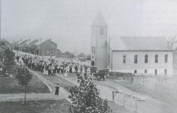 Image of the church, people standing outside, and company housing can be seen in the background.