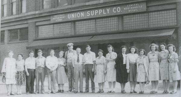 A row of men and women pose for a photograph in front of the Company store.
