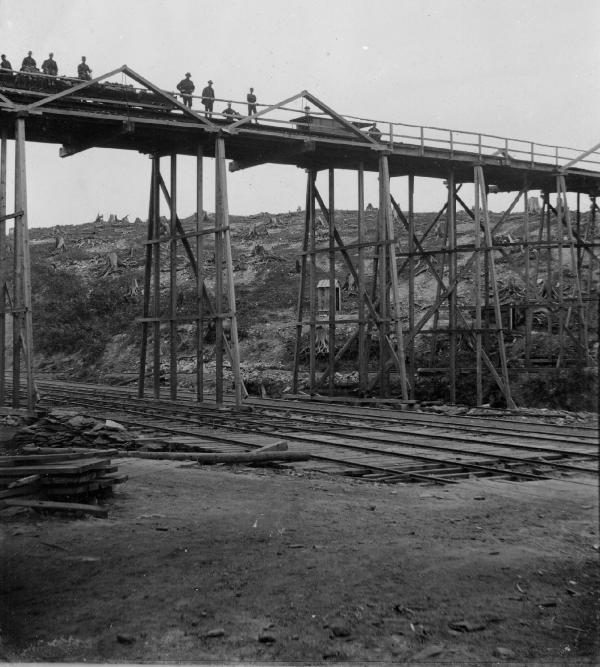 Men standing along the top of the trestle pose for a photograph.