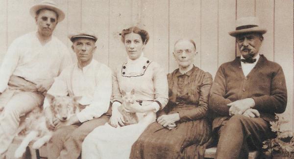 Image of the Landis family sitting on a bench. The two brothers, with their sister, mother, and father, as well as the family dog and cat. 