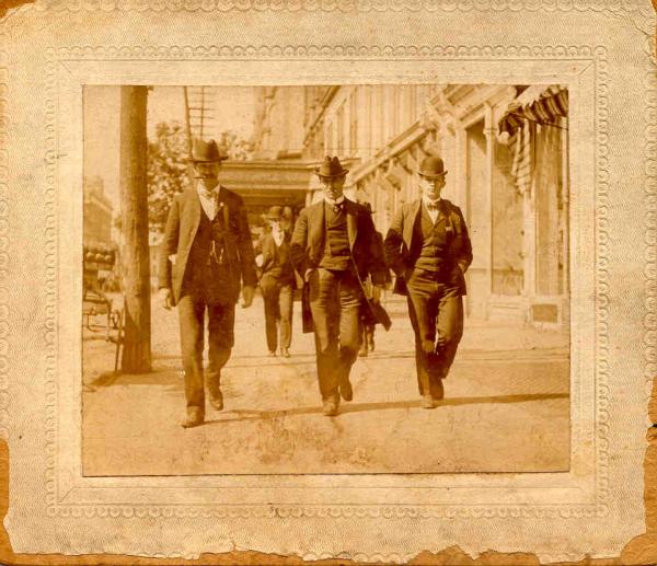 Men walk down a city street. Left to right:  George W. Harltein, (Secretary, District 9) John Mitchell, Mr. Barrett (Reporter, Scranton Truth) May 7, 1902. 