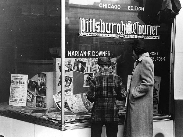 Photograph of a window of the Pittsburgh Courier and a woman and child look inside.