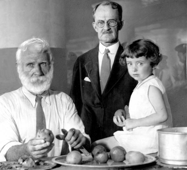 This publicity photo shows Philadelphia Mayor J. Hampton Moore peeling a potato, as Ernest Gray, age 81, and  Jean Helmstreet, age three pose next to him, at the Shelter for Homeless Men kitchen.