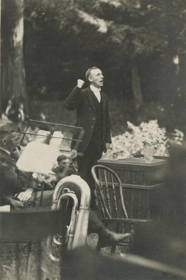 Photograph of John Brophy, arm raised in the air and his fist clenched, speaking at an outdoor gathering.