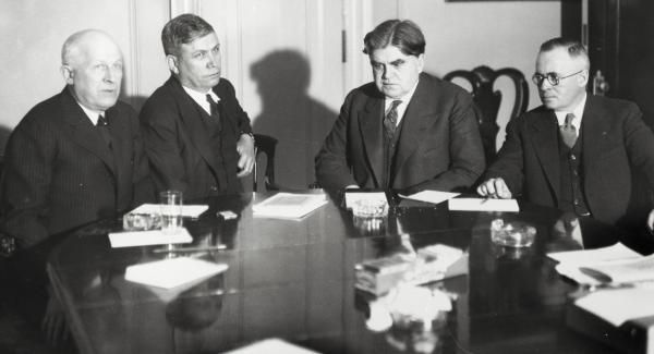 Four men dressed in suits sit at a table.