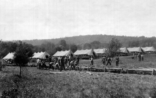 CCC workers strip bark from logs. Camp tents apparent in background.