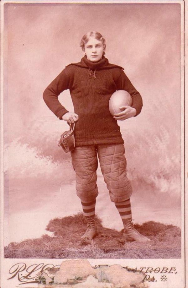 A young man in a uniform posing with a football in his hand.