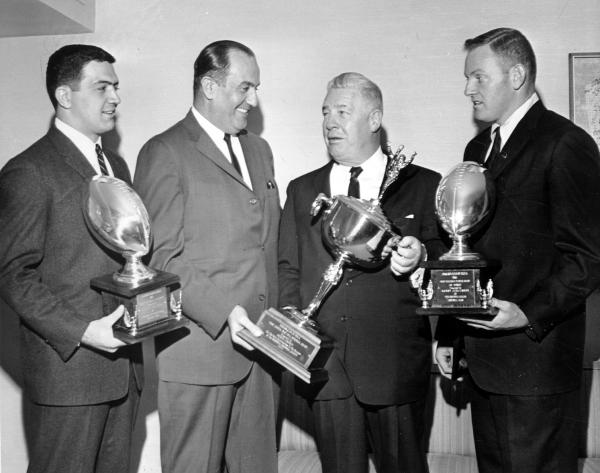Art Rooney receiving the Bert Bell Man of the Year Award. Four men dressed in suits and holding trophys pose for picture. 