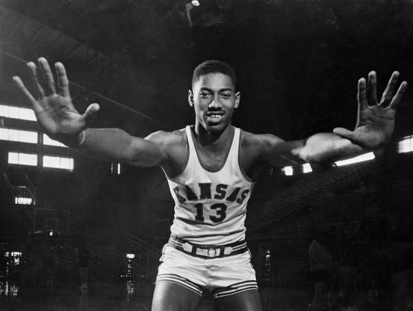 A man in a basketball uniform stretches his arms forward to demonstrate the size of his hands. 