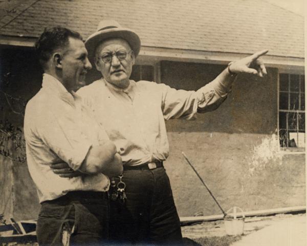 Two men standing next to each other are engaged in a discussion. The older gentleman is pointing.