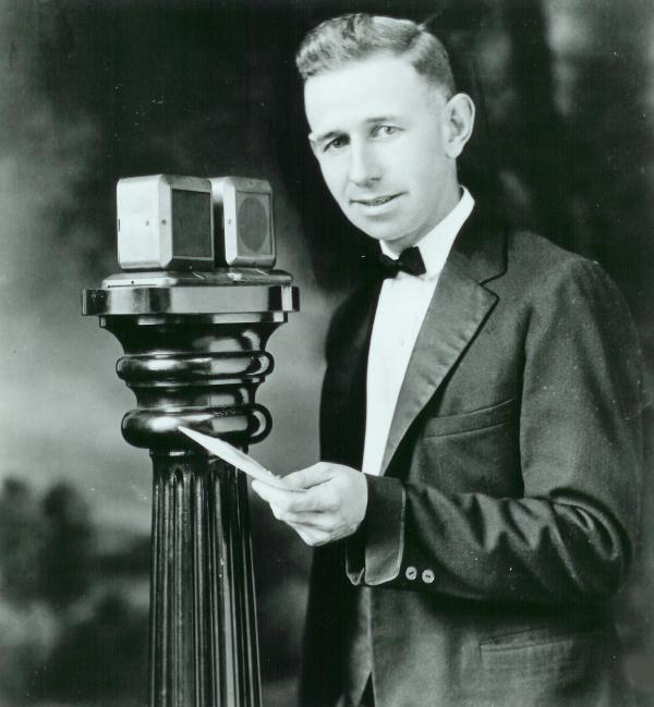 A man dressed in a suit stands at a microphone.