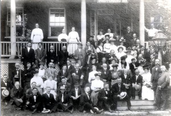 Group photograph of a men and women in front of a lodge, posing on the porch and steps for a photo.