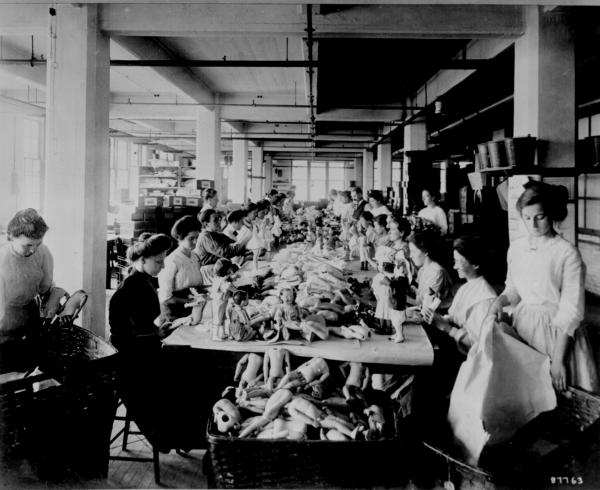 Women assembling dolls on a long worktable at the Shrenhat Toy Company 