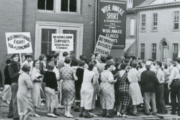 Women walk the picket lines in front of the factory carrying signs that read: Fight for the living wage, Beware Bosses speeches, and Reading Labor Supports Wide Awake Strikers. 