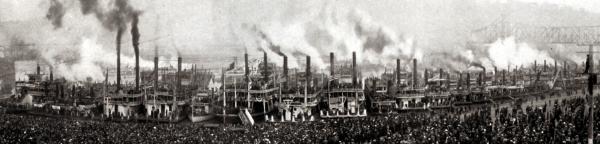 An image of a long line of steam ships docked and a huge crowd in the foreground.