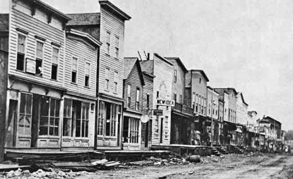 A photograph of a row of storefronts along a dirt road, the first five of which appear to be empty.