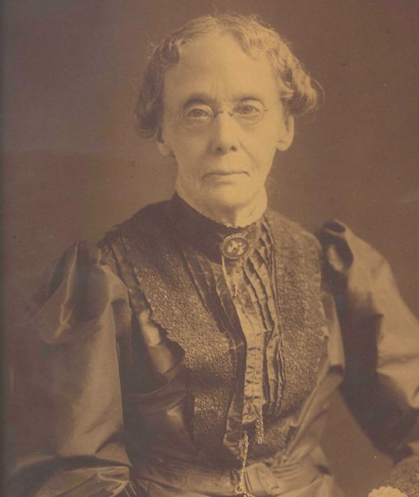 Sepia photgraph of an elderly lady. She is wearing a dress with a ruffled front and spectacles.