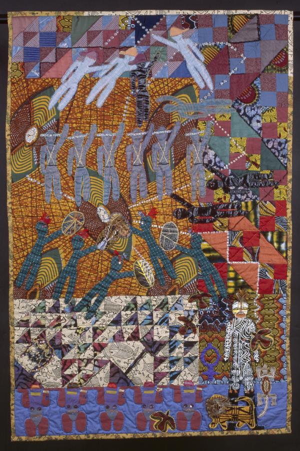 A colorful story quilt, with rich oranges, reds, purples and blues. Figures of people, a lion, a lizard, and birds are stitched into the quilt. 