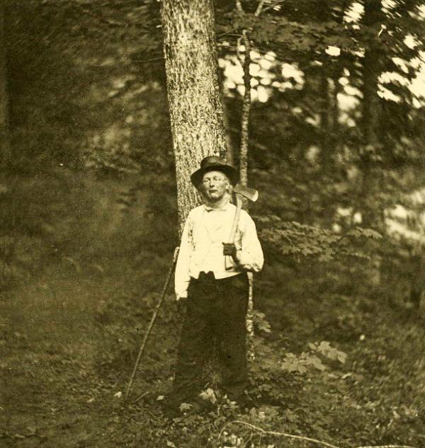 Image of Greeley in the woods holding an axe over his shoulder.