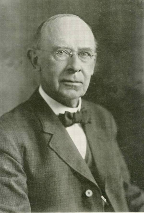 Black and white, head and shoulders photograph of a balding man, wearing a suit, shirt, and bowtie.