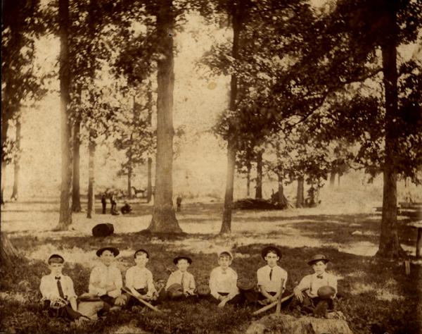 Photo of boys sitting under trees with baseball mitts and bats (circa 1890).   
