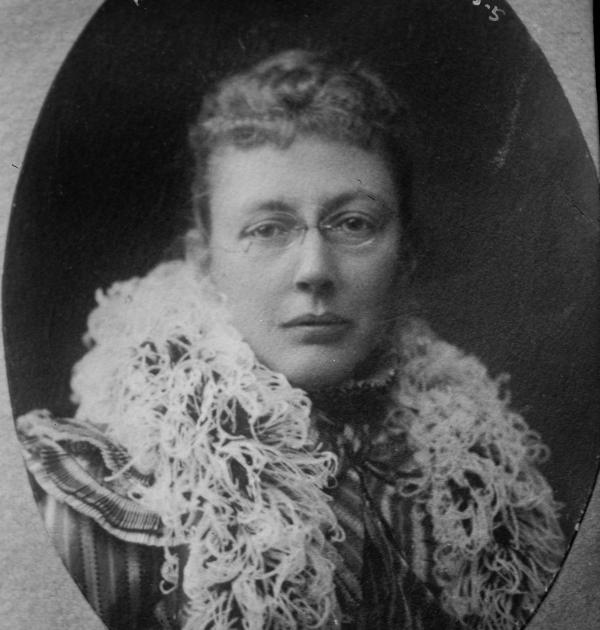 Head and shoulders image of a woman wearing glasses and a feathered wrap 