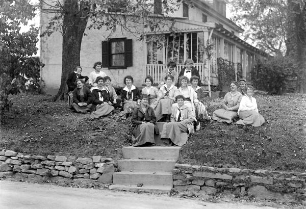 Female students sitting on the steps and slope of bank in front of the school.