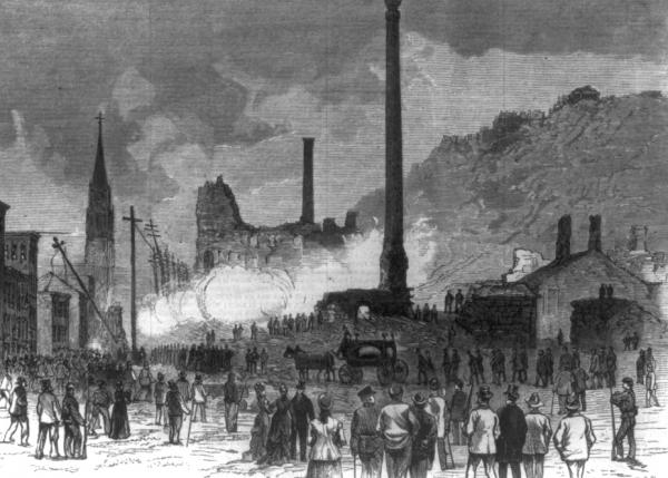 A funeral procession and a horse drawn hearse are the focus of this image, while the buildings still  spew smoke from the fires. 