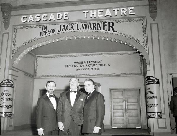 On the evening of his tribute dinner, Jack Warner (center), retiring co-founder of Warner Brothers Studios, stands with the company's chief executive officer, Ted Ashley (left), and an unidentified friend in front of the Cascade Theater in Hollywood, California.