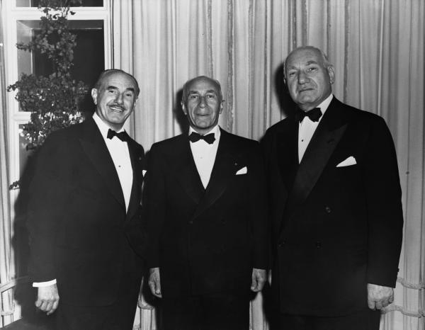 Image of the three brothers dressed in suits, standing against a curtain backdrop.