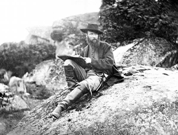 Photograph of Waud as he sits on a boulder with a sketch book propped on his knee.
