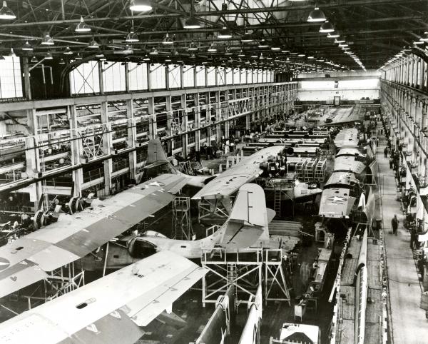 Interior photograph of a Naval aircraft factory filled with planes and employees