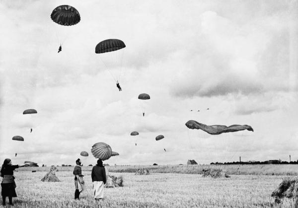 German women pause in their harvesting to watch the landing of paratroopers   
