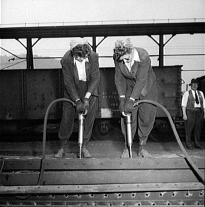 Two women dismantling the side of an old hopper car.