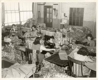 A room of female seamstresses sew parachutes for the war effort.