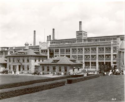 Hershey Chocolate Factory, Exterior; west end, ca. 1925. Shows employees leaving; cars; grass in foreground
