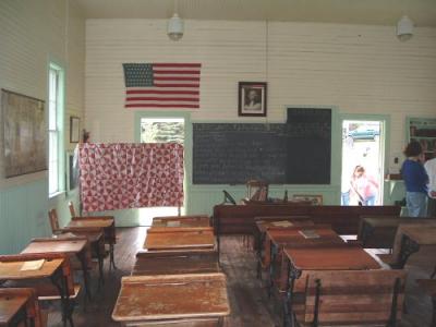 Color modern-day photo of interior view of Daggett One-Room School. It shows blackboard, flag, and portrait of George Washington.