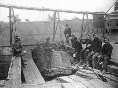 Anthracite mineworkers at a shift change. A crew prepares to enter a mine; the crew that just completed their shift pose nearby. Like the coal they mined, they were transported in the mine via coal cars.