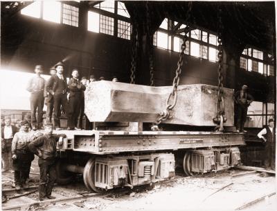Homestead Steel Works and workers standing next to a railroad flat car that carries a large steel product.
