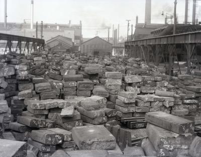 Photograph shows piles of steel ingots on the exterior of the steel plant.