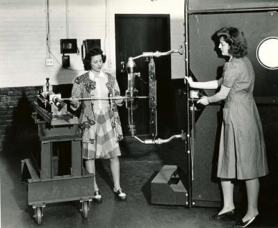 Two women pose with machinery for publicity photograph.