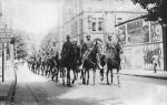 A large group of mounted police ride down the middle of the road in threes.