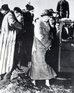 Eleanor Roosevelt stands about to enter an automobile. Doris Duke, tobacco heiress wearing a black coat, and others stand behind her. 