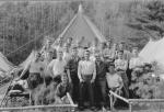 Group photograph of men posed outside of a tent.
