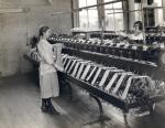Two young women standing in front of machines in a silk mill factory wind the silk around their hands.