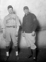 Two men standing side by side. The younger one wears a baseball uniform.