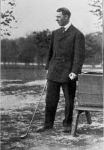 Photograph of a man standing and holding a golf club. 