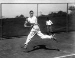 Tennis champion Bill Tilden in motion, stretching  as he hits a return ball with his racket. 