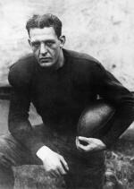 A man in uniform kneels while holding a football.