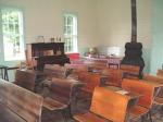Interior image of Daggett Schoolhouse. Desks, a globe, a heater, and a piano are all visible.
